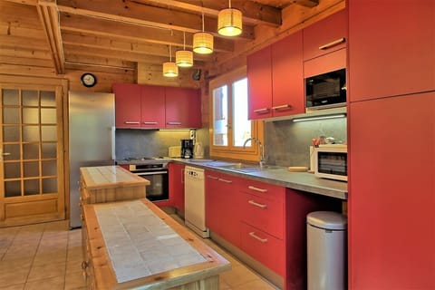 The chalet's fully equipped kitchen boasts modern appliances and a sleek design, featuring a breakfast bar with tiled countertop, a dishwasher, a microwave, and a bright red color scheme that adds a touch of vibrancy to the space. The kitchen offers a wel