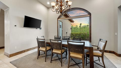 Elegant dining area with a glass-top table, arched window, and chandelier.