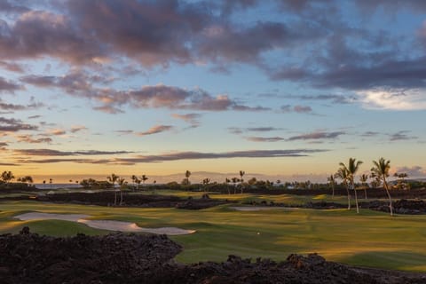 This serene golf course view captures the essence of a tranquil evening, with lush fairways framed by volcanic rock under a spectacular sunset sky.