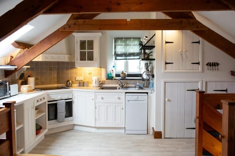 kitchen area with white cupboards and wall cupboard. oven, dishwasher, kettle and microwave