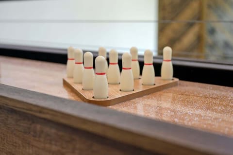 Mini bowling pins setup on a rustic shuffleboard table for fun family games in a stylish indoor loft area.