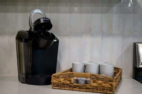 Keurig coffee maker on white quartz countertop with wicker tray, white mugs, and coffee pods in a modern kitchen coffee station setup.