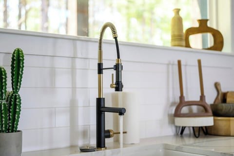 Stylish black and gold kitchen faucet with running water, surrounded by modern decor and natural light.