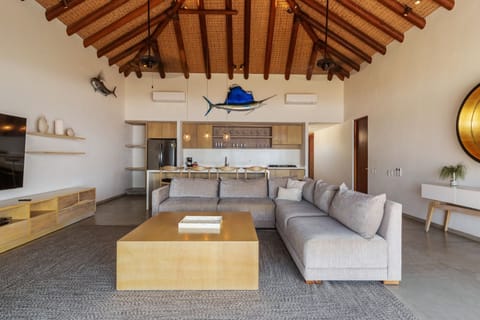 A warm and inviting living area with high ceilings, natural wood accents, and an open layout leading to the kitchen.