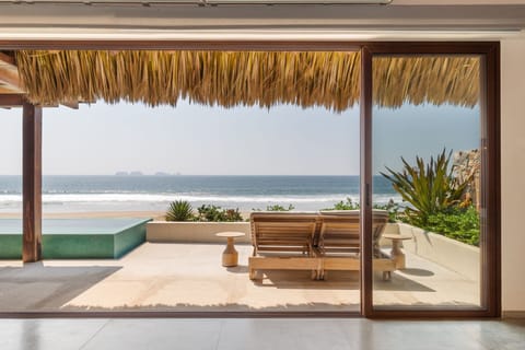 Relax in this stunning beachfront lounge area, featuring a shaded pergola, ocean views, and cozy seating.
