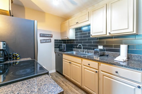 A modern kitchen with granite countertops, white cabinets, a black tiled backsplash, and stainless steel appliances, including a refrigerator and an electric stovetop.