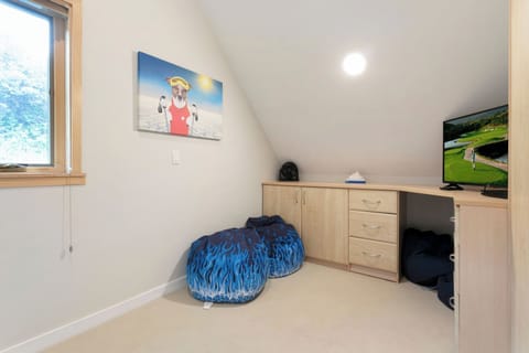 A small room with slanted ceilings featuring a cabinet with drawers, a television showing a golfing scene, two bean bags with blue patterns, and a painting of a dog on the wall.