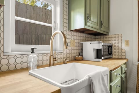 - Chic farmhouse-style sink with gold-tone faucet adds elegance to the kitchen
- Retro sage-green cabinets and hex-tile backsplash offer classic style
- Essentials like a Keurig, microwave, and bright natural light await