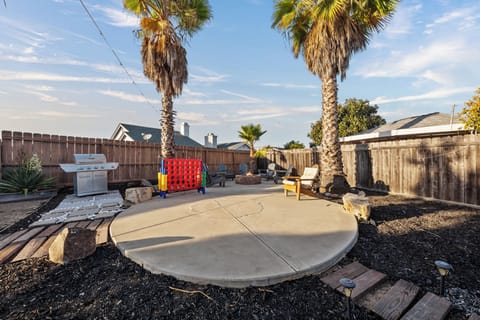 Backyard with firepit, play area, BBQ, loungers, palm trees, and studio.