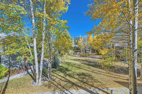 A serene autumn landscape with trees shedding yellow leaves, a grassy area, and clear blue sky in the background.