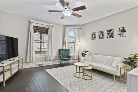 Bright living room featuring a large window with stylish curtains, a chandelier ceiling fan, an elegant sofa, tasteful decorations, mini side tables, and a polished, sophisticated floor design—perfectly blending comfort and modern elegance