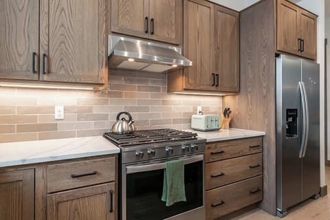 - Sleek cooking area with a gas range and stainless steel hood vent
- Warm wood cabinetry pairs with a neutral backsplash for a timeless look
- Convenient storage and modern appliances make meal prep effortless
