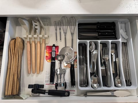 Fully stocked kitchen drawer with whisks, pizza cutter, ladles, and cutlery sets