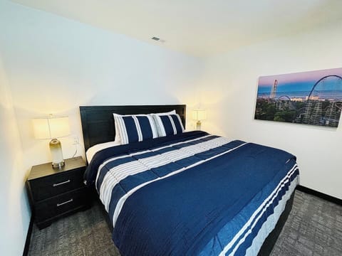 A cozy bedroom featuring a plush bed with crisp blue and white striped bedding, complemented by matching nightstands and vibrant artwork that brings a modern touch to the serene space.