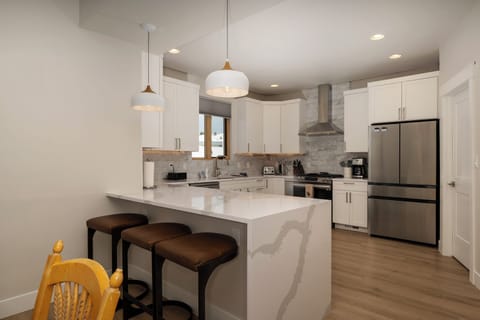 - Sleek, modern kitchen featuring a large island with bar seating for three - Stainless steel appliances and stone countertops add a touch of style - Pendant lights above the island create an inviting atmosphere for casual meals