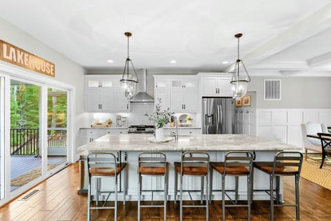 A spacious and modern kitchen with a large marble island, high-end appliances, elegant pendant lighting, and open access to the dining and living areas with views of the backyard.