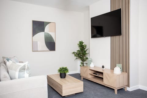 A cozy living room with a soft sofa, a TV mounted on the wall, a simple wooden coffee table, and a decorative potted plant.