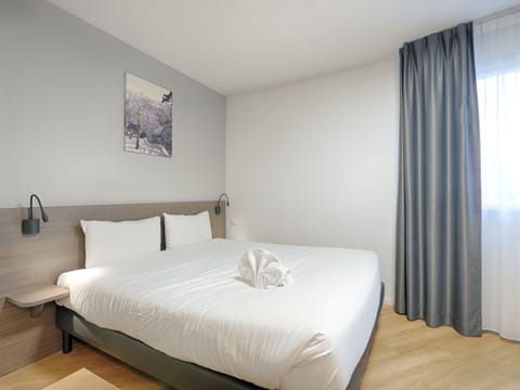 Spacious studio bedroom with the option of a double bed or two single beds, complemented by soft lighting and natural light from large windows.