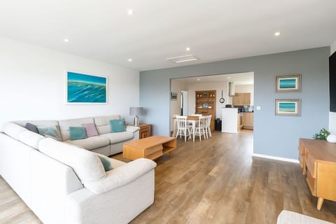 Living area with corner sofa and chairs seating eight, 46 inch Smart TV with Sky package. Patio doors with distant sea views