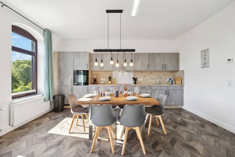 Moderne Küche mit grauen Fronten, Holzarbeitsfläche und stilvoller Hängelampe über dem gedeckten Esstisch.