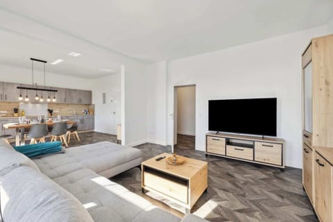 Großzügiger Wohn- und Essbereich mit gemütlichem Sofa, modernem TV und offener Küche samt Esstisch.