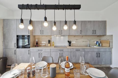 Moderne Küche mit grauen Fronten, Holzarbeitsfläche und stilvoller Hängelampe über dem gedeckten Esstisch.