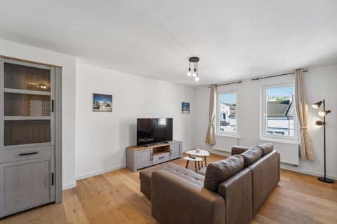 Das Wohnzimmer überzeugt mit einer gemütlichen Couch, einem modernen Flachbild-TV, stilvollen Holzmöbeln und großen Fenstern, die den Raum mit Tageslicht durchfluten.