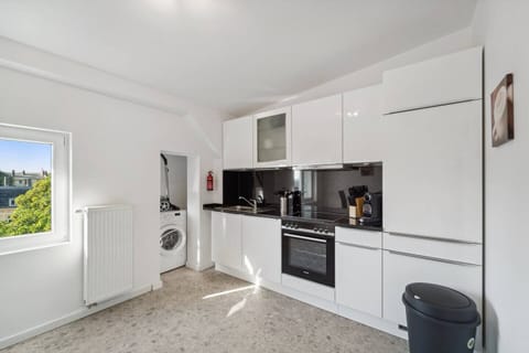 Die moderne Küche überzeugt mit glänzend weißen Fronten, schwarzer Arbeitsplatte, vollständiger Ausstattung und einer praktischen Waschmaschine in der Nische.