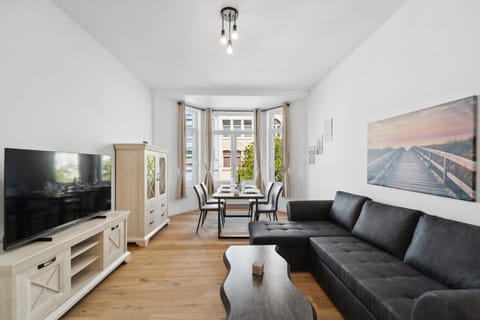 Das stilvolle Wohnzimmer in Wilhelmshaven beeindruckt mit großer Fensterfront, gemütlichem Ecksofa, modernem TV-Bereich und elegantem Essplatz im Erker.
