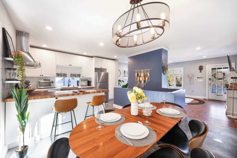 A wide shot showcasing the open layout of the kitchen and dining area, with a wood-top island, bar stools, and a large decorative light fixture. The navy accent wall adds depth to the room.