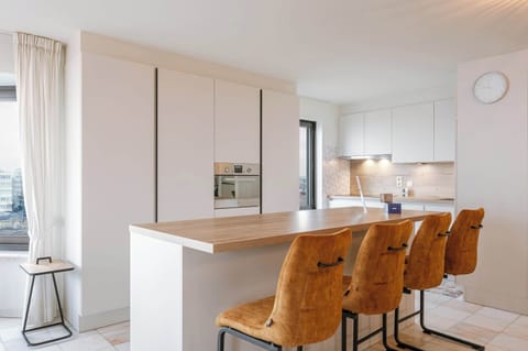 Modern open kitchen with ocean views. Features a sleek island, stylish barstools, and warm lighting, creating a bright and inviting space.