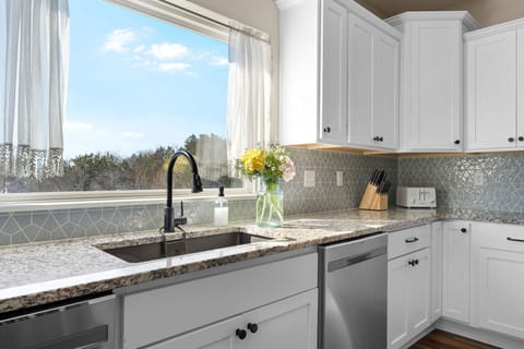 - Wash up or prep a meal with a peaceful view of trees and sky just beyond the window
- Let the sunlight pour in while you enjoy the little touches like flowers and soft curtains
- Every part of this kitchen brings calm, charm, and a homey feel