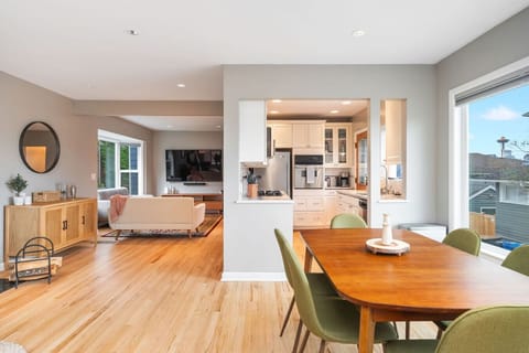 MAIN FLOOR-DINING ROOM: A sleek wooden table with six olive-green chairs sits by a large window, filling the space with natural light. The open layout connects seamlessly to the kitchen with the dining room.