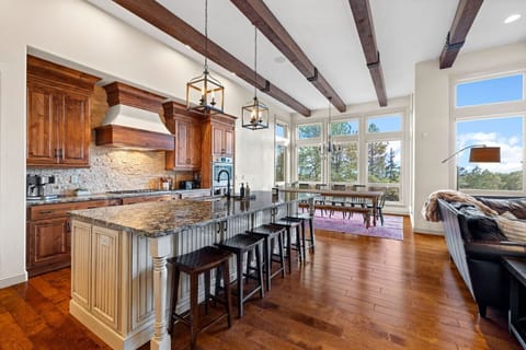 This open-concept gathering space brings everyone together with ease—from morning coffee at the granite island to shared meals at the farmhouse-style dining table, all framed by soaring windows and forest views. Whether you're cooking, dining, or lounging