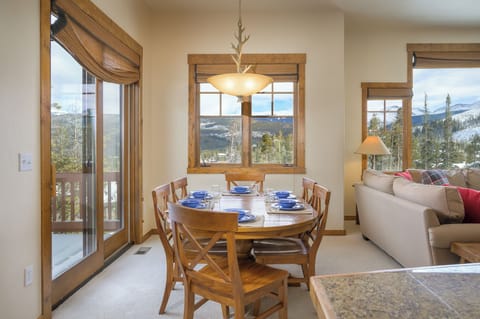 - Dining area with round wooden table set for six overlooks scenic mountain views - Large windows and sliding glass doors brighten the space with natural light - Cozy setup makes it perfect for family meals in an inviting alpine atmosphere