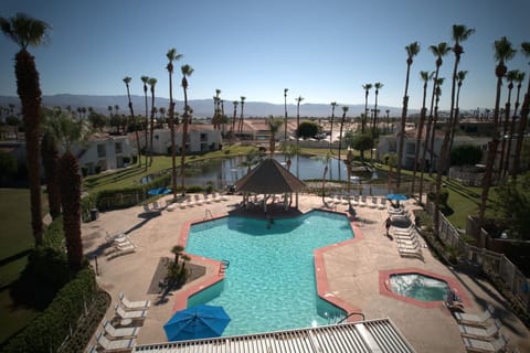 A stunning view from above showcases the expansive pool area, complete with a tiki hut and scenic lakeside setting, ideal for relaxing under the sun.