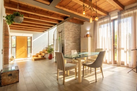 Spacious living room with an elegant and bright dining area, featuring exposed beams and large windows overlooking the garden. The space combines rustic warmth and modern design, creating a welcoming and refined space to relax or share meals with the family.