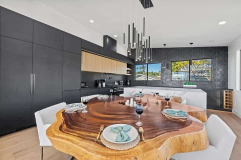 A live-edge table takes center stage, complemented by contemporary seating and minimalist lighting. Black cabinetry with fluted wood-finished cupboards and wood-designed floors create a warm yet modern atmosphere.