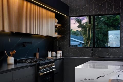 Designed with precision and style, with built-in modern kitchen appliances, this kitchen combines bold black cabinetry, warm natural wood accents, and a sleek white waterfall island for the perfect balance of modern luxury.