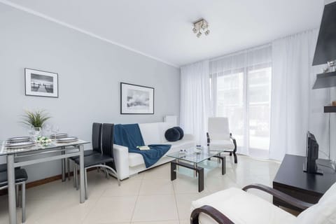 A bright room with a sofa, coffee table, and a large window. A TV is visible in the background.