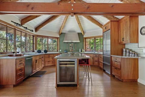 Spacious, unique kitchen with an octagonal vaulted ceiling, exposed wooden beams, warm wooden cabinetry, and abundant natural light from surrounding windows.