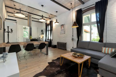 A cozy open-plan living room with a stylish black sofa and a dining area. Natural light streams in through large windows.