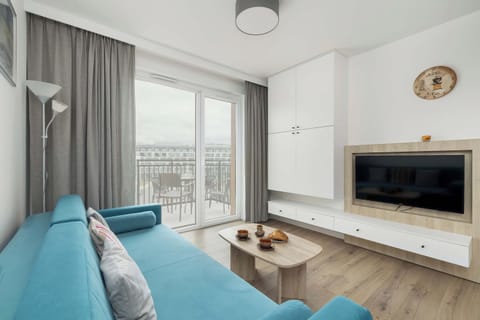 The spacious living room impresses with a comfortable blue sofa, a large TV hanging on the wall and light, delicate curtains that let in plenty of natural light, creating a cozy atmosphere.