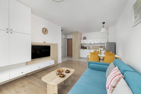 A panoramic view of the living room shows a lounge area with a comfortable sofa and wall-mounted TV, as well as a functional kitchenette, creating a cohesive and comfortable whole.