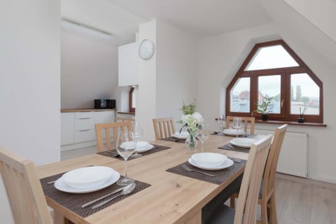A wooden table, with six chairs and a cover, located in a bright dining room with a view of the surrounding area.