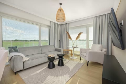 A bright living room with light gray sofas, a round coffee table, and a scenic view through floor-to-ceiling windows.