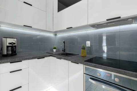Fully equipped kitchenette with sleek white cabinetry and black backsplash.