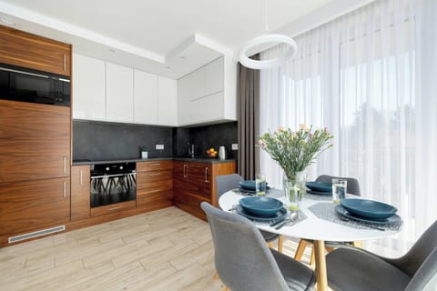 An elegant kitchenette with white cabinets, a black countertop and modern appliances will allow you to prepare delicious meals. Large windows with transparent curtains let in plenty of natural light, creating a cozy atmosphere. 