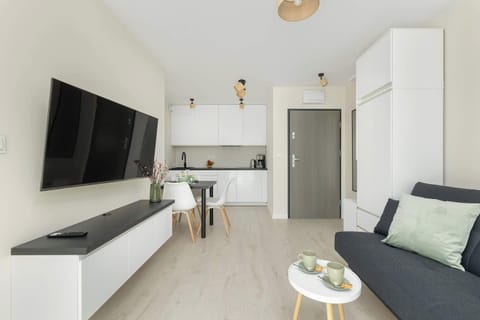 A bright living room with a stylish sofa, a TV, and a dining table. The modern decor creates a cozy and inviting atmosphere.