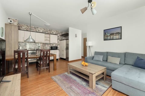 A cozy living room with a sectional sofa, a rug, and a wooden dining table set for four, blending comfort with functionality.